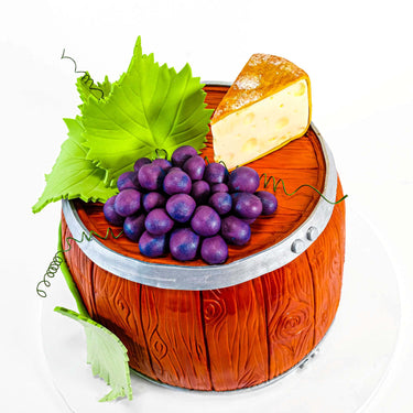 Wine Barrel Cake made to look like a wooden barrel, with fondant grapes, leaves and a cheese wedge