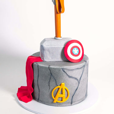 Two tier stone effect Marvel Avengers Cake with Thor's hammer, a red cape, shield and Avengers logo