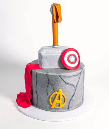 Two tier stone effect Marvel Avengers Cake with Thor's hammer, a red cape, shield and Avengers logo