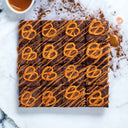 Salted Caramel Brownies topped with salted pretzels and caramel drizzle, on marble