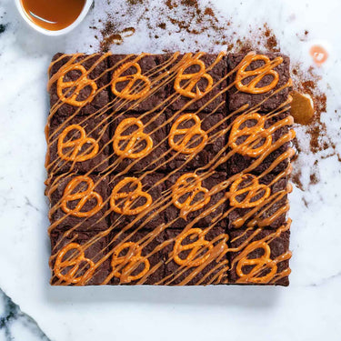 Salted Caramel Brownies topped with salted pretzels and caramel drizzle, on marble