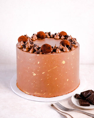 Triple Chocolate Cake topped with chocolate truffles, buttercream swirls and gold splatters, next to squares of dark chocolate