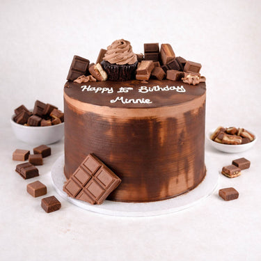 Chocolate Overload Cake topped with chocolate bars, a cupcake and chocolate bites, with a piped birthday message