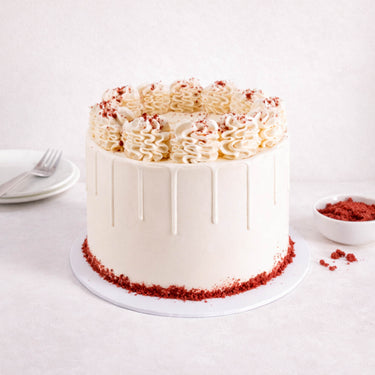 Red Velvet Cake with smooth white buttercream, piped swirls and red velvet crumbs around the edge