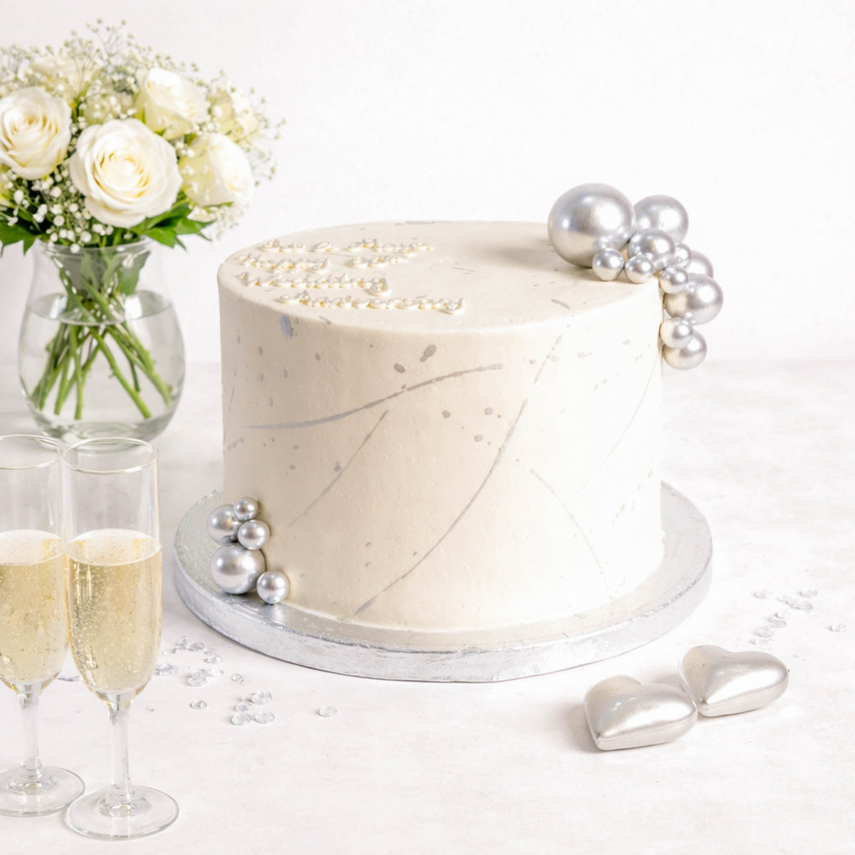 Free From Silver Cake with off white icing and silver pearls, with champagne flutes and white roses