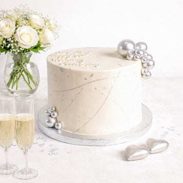 Silver Cake with silver pearls and hearts, next to champagne flutes and white roses