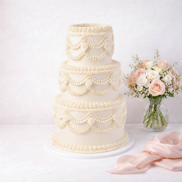 Frilly Wedding Cake: Elegant three-tiered cake with piped frosting swags, accompanied by a vase of roses, embodying vintage charm for special occasions.