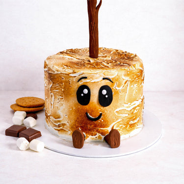 Gluten free Free From Toasted Marshmallow Cake with a cartoon face, feet and stick, with marshmallows