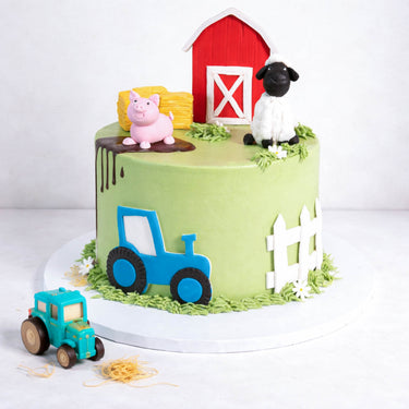 Farm Cake with a fondant barn, sheep, pig, hay bales and piped grass, with a toy tractor