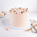 Carrot Cake with blush pink buttercream, biscuit pieces and edible petals, next to a slice on a plate