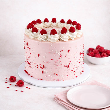 Raspberry White Chocolate Cake with pink buttercream, fresh raspberries, rosettes and heart sprinkles