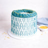 Stencil Cake with a teal leaf pattern and yellow sugar pearls, on a white cake board