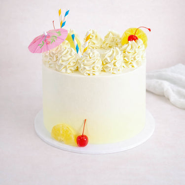 8 inch Cocktail Cake with white buttercream, rosettes, pineapple, cherries, paper straws and a cocktail umbrella