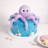 Mini Under The Sea Cake with blue buttercream and a purple fondant octopus, next to shell shaped biscuits
