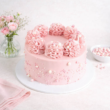 Mini Rose and Elderflower Cake with pink rosettes and sugar pearls, next to a vase of pink roses
