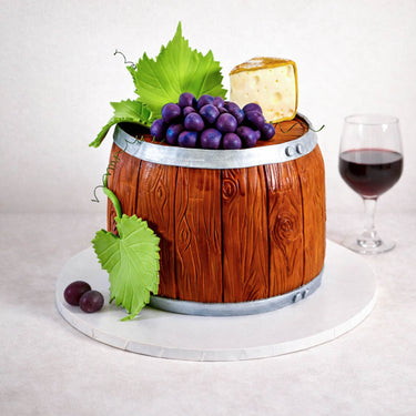 Free From Wine Barrel Cake with fondant grapes, cheese and vine leaves, next to a glass of red wine