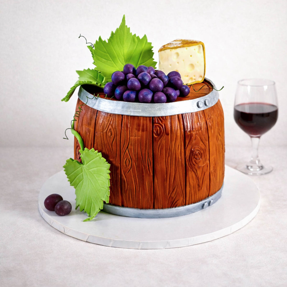 Free From Wine Barrel Cake with fondant grapes, cheese and vine leaves, next to a glass of red wine