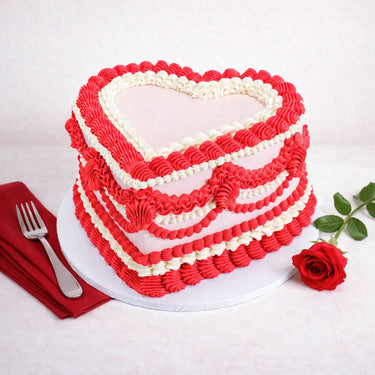 Pale pink Frilly Heart Cake with red and white piped frills, next to a red rose