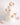 Rustic Wedding Cake with white frosting, pink roses, and greenery on a table with champagne, dessert plates, and blush macarons. Perfect for elegant weddings.