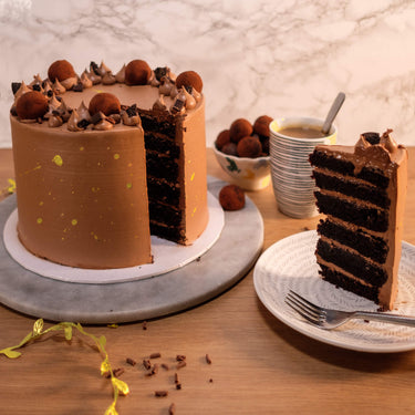 Triple Chocolate Cake with a slice cut out showing chocolate sponge layers, served with a cup of coffee