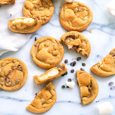 S'mores Cookies with chocolate chips and marshmallow pieces, whole and broken, on stone