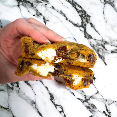 Hand holding a S'mores Cookie broken in half, showing chocolate and melted marshmallow
