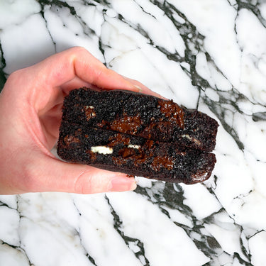 Hand holding a Triple Chocolate Cookie broken in half, showing melted chocolate