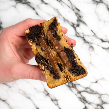 Hand holding a Hazelnut Marble Cookie broken in half, showing a melted chocolate centre