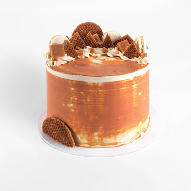 Salted Caramel Cake with caramel buttercream, cream swirls, stroopwafels and macarons on a white background