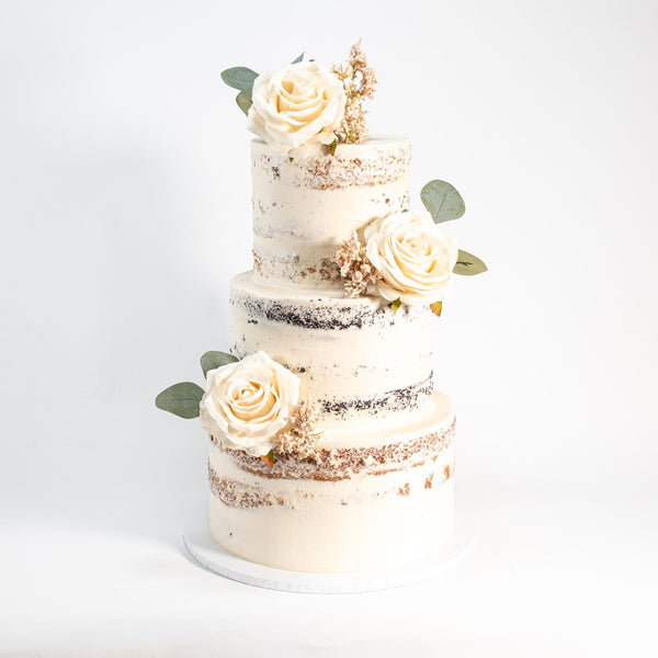 Three-tier Naked Wedding Cake with ivory roses, filler flowers, and eucalyptus leaves, lightly frosted for a rustic finish, highlighting Harry Batten's artisan craftsmanship.
