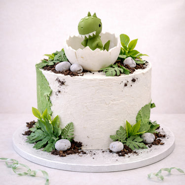 Baby Dino Cake with a green dinosaur hatching from an egg, on a mossy forest scene with chocolate soil