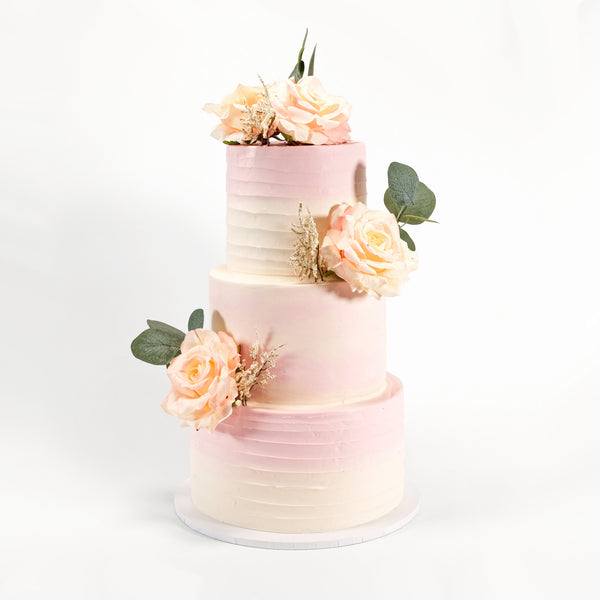 Ombré Wedding Cake with ivory-to-blush buttercream, adorned with peach roses and foliage, crafted by Harry Batten, highlighting handmade elegance and personalization.