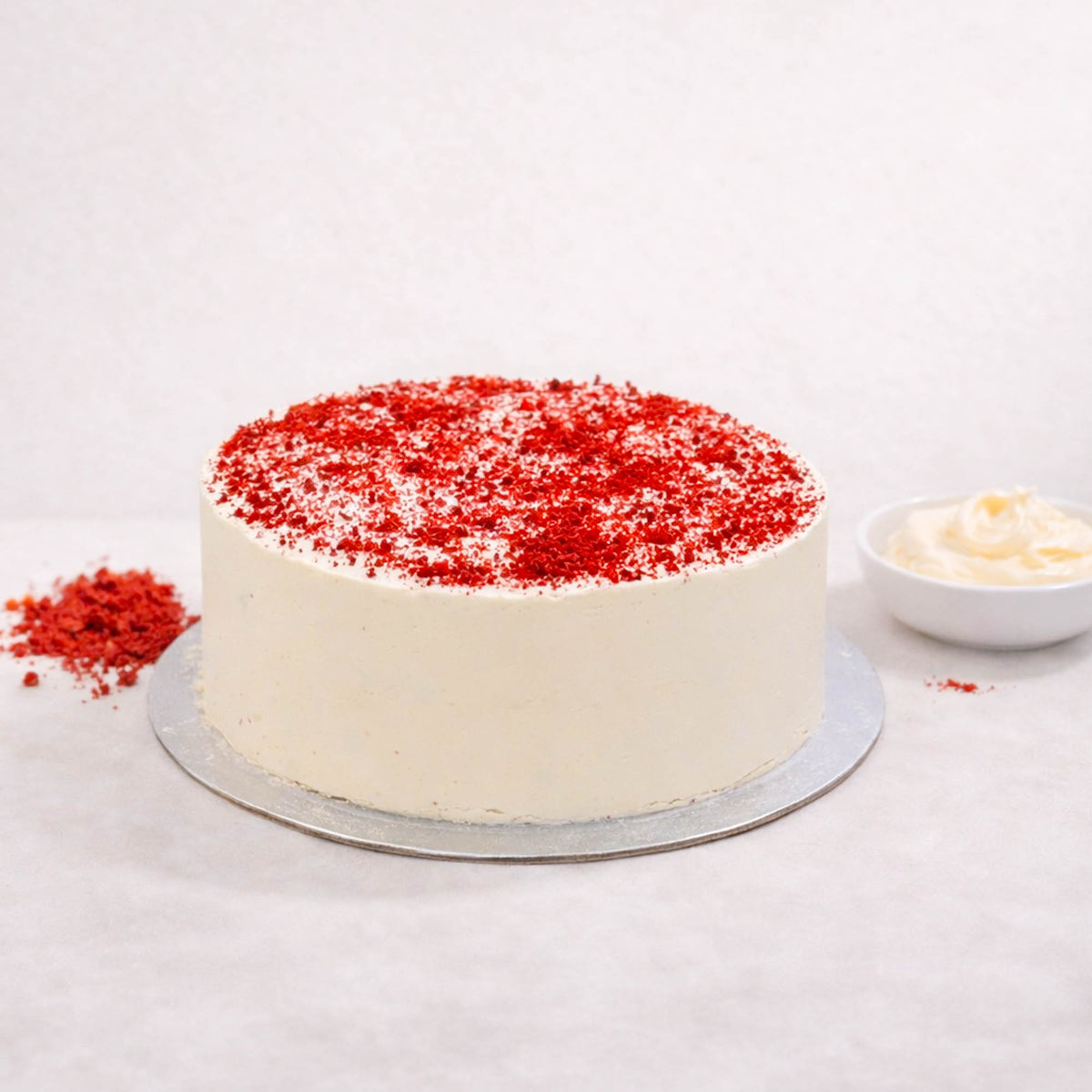 Red Velvet Cake with smooth white buttercream and red velvet crumbs on a silver board