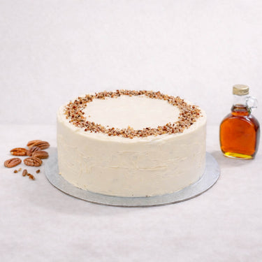 Maple and Pecan Cake with ivory buttercream topped with pecans, next to maple syrup