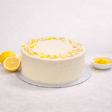 Lemon Drizzle Cake with lemon curd and meringue crumbs, next to lemons and zest