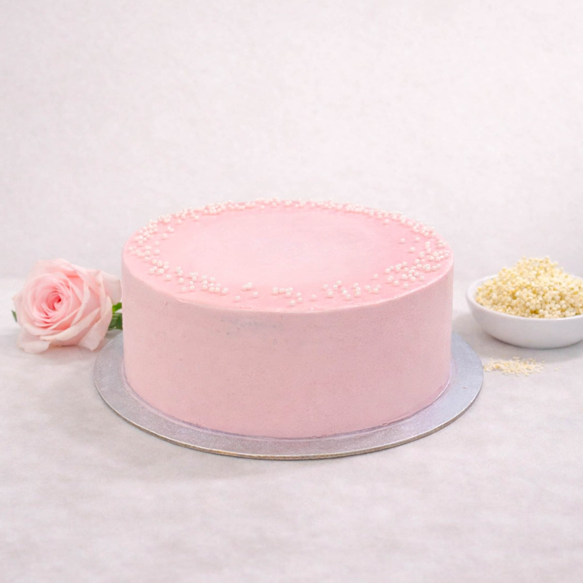 Rose and Elderflower Cake with pale pink buttercream and white sugar pearls, next to a rose