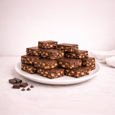 Wholesale Tiffin bars on a plate, showcasing smooth chocolate tops with nut-studded fillings. Extra chocolate pieces on the side enhance the indulgent presentation.