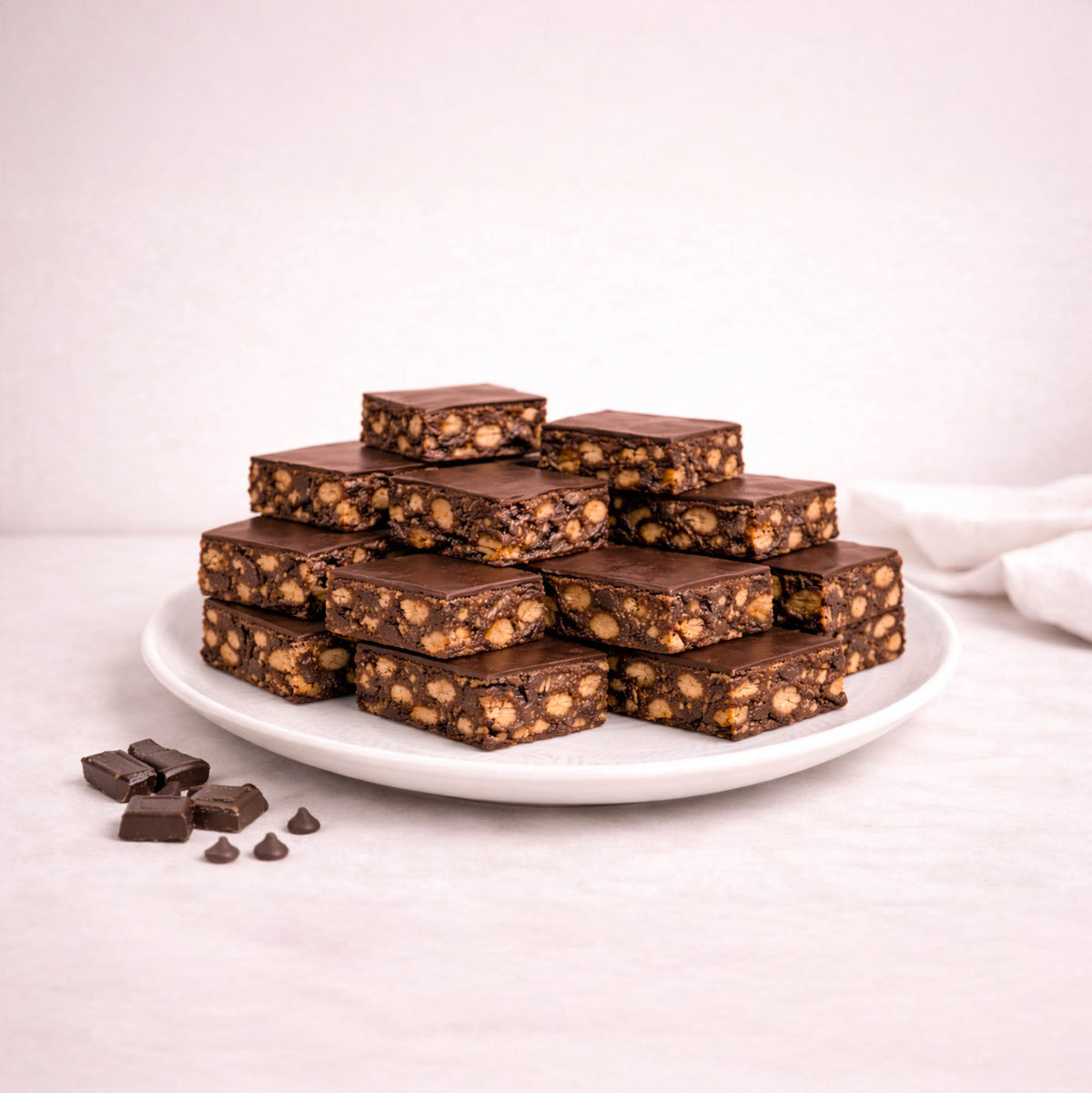 Wholesale Tiffin bars on a plate, showcasing smooth chocolate tops with nut-studded fillings. Extra chocolate pieces on the side enhance the indulgent presentation.
