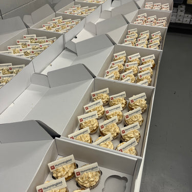 Boxes of branded cupcakes with buttercream, gold sprinkles and edible logo plaques, ready for delivery