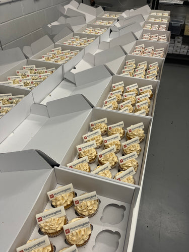 Boxes of branded cupcakes with buttercream, gold sprinkles and edible logo plaques, ready for delivery