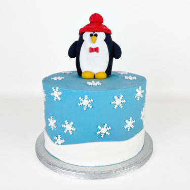 Penguin Cake with sky blue fondant, snowflakes and a fondant penguin in a red hat